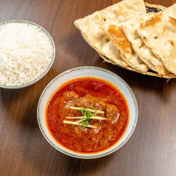 A bowl of red curry with ginger and herbs, a bowl of white rice, and naan bread.