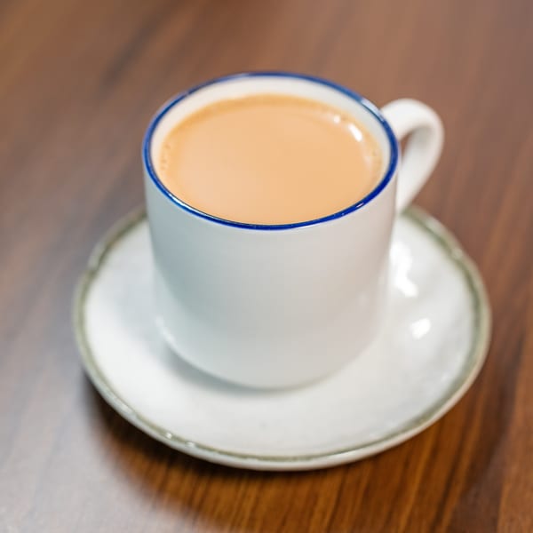 A white mug with a blue rim, filled with chai tea, sits on a saucer.