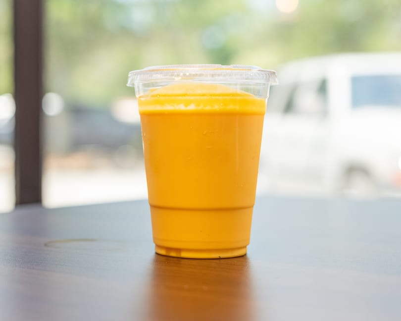 A vibrant orange Thai iced tea in a clear plastic cup sits on a dark wooden table.