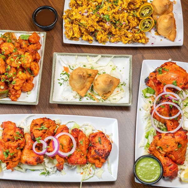 An overhead view of a wooden table laden with various Indian dishes, including samosas and tandoori chicken.