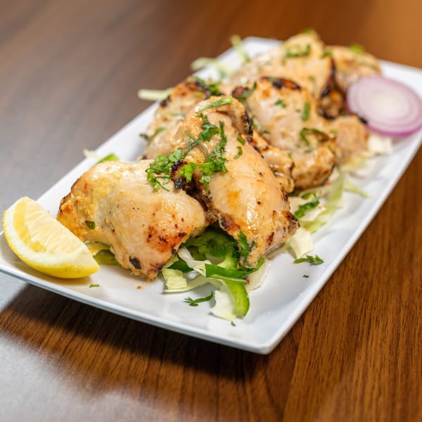 Grilled chicken pieces with herbs, lemon, and red onion on a white plate.