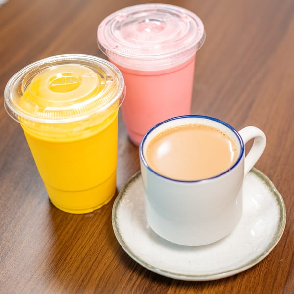 Three drinks on a wooden table: a yellow smoothie, a pink smoothie, and a cup of chai.