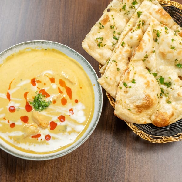 Creamy yellow curry with red oil swirls and cilantro, served with a basket of naan bread.
