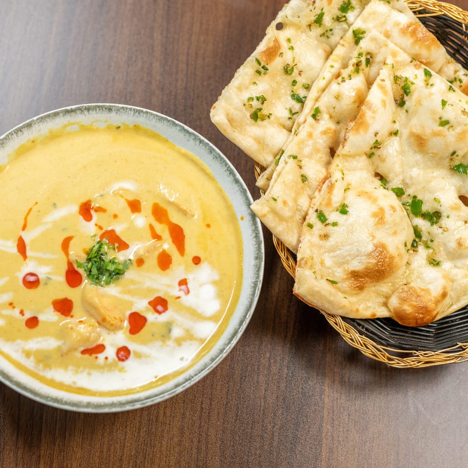 Creamy yellow curry with red oil swirls and cilantro, served with a basket of naan bread.