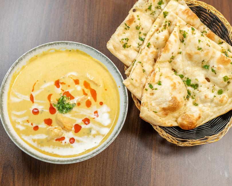 Creamy yellow curry with red oil swirls and cilantro, served with a basket of naan bread.