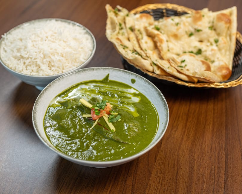 Palak Paneer with rice and naan bread on a wooden table.