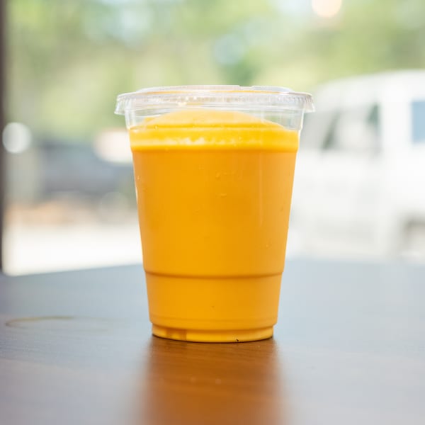 A vibrant orange Thai iced tea in a clear plastic cup sits on a dark wooden table.
