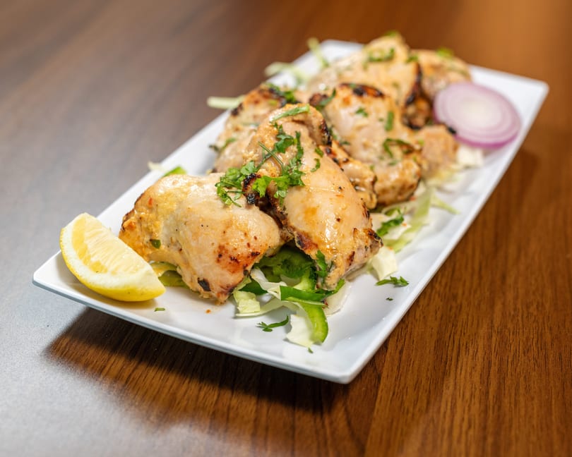 Grilled chicken pieces with herbs, lemon, and red onion on a white plate.