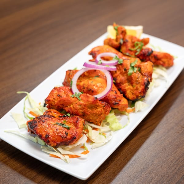 Tandoori chicken tikka, garnished with red onion and cilantro, served on a bed of lettuce.
