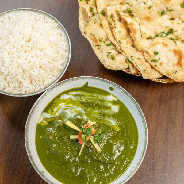 Indian meal with palak paneer, white rice, and garlic naan on a wooden table.