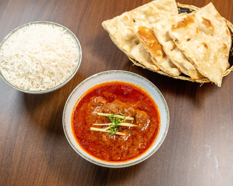 A bowl of red curry with ginger and herbs, a bowl of white rice, and naan bread.