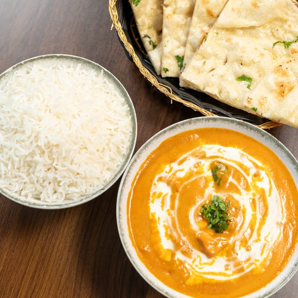 Indian butter chicken with rice and naan bread on a wooden table.
