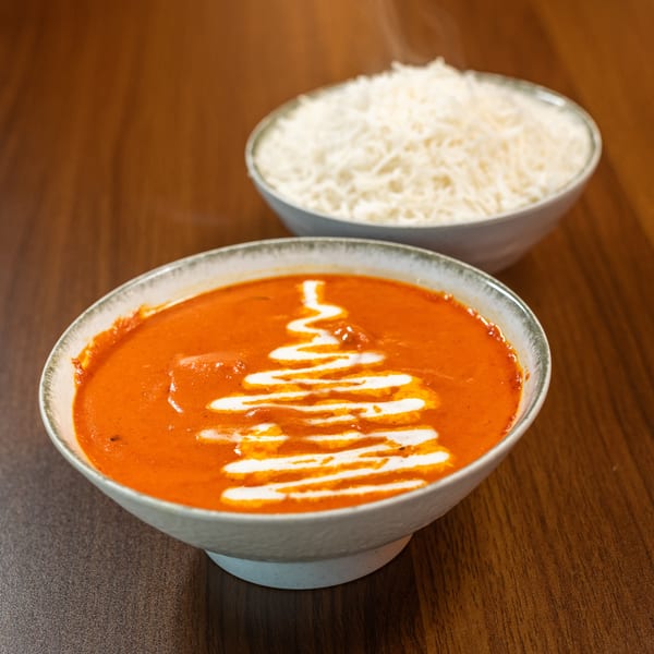 A bowl of orange curry with a white cream swirl, and a bowl of white rice.