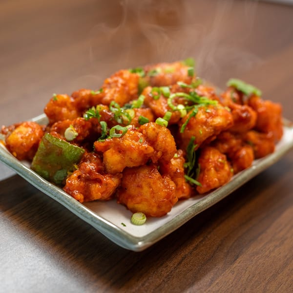 Steaming hot Gobi Manchurian, garnished with green onions and bell peppers, on a white plate.