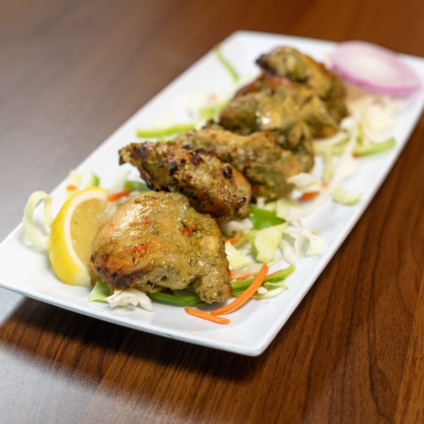 Green-marinated chicken pieces with lemon, red onion, and shredded vegetables on a white plate.