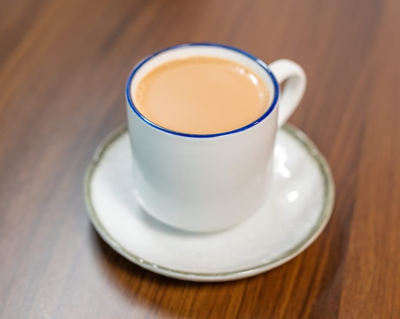 A white mug with a blue rim filled with chai tea, on a matching saucer.