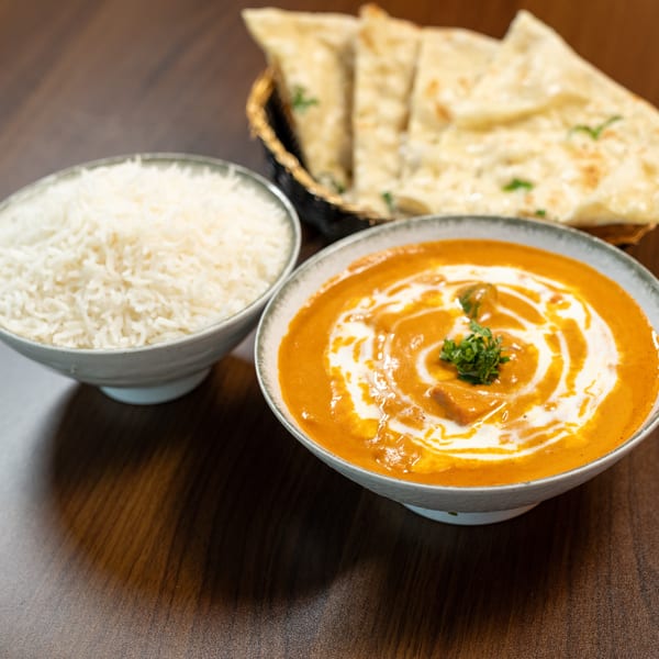 Indian butter chicken with rice and naan bread on a dark wooden table.