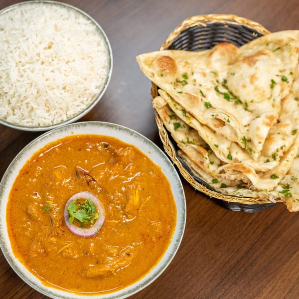 Indian curry with rice and a basket of naan bread on a wooden table.