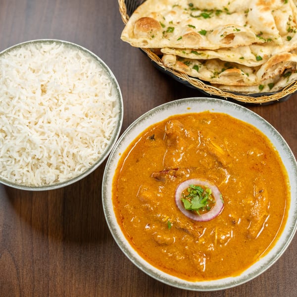 Indian curry with rice and naan bread on a wooden table.