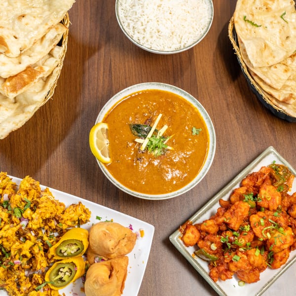 Overhead view of a spread of Indian dishes including curry, rice, naan, pakora, and chili paneer.
